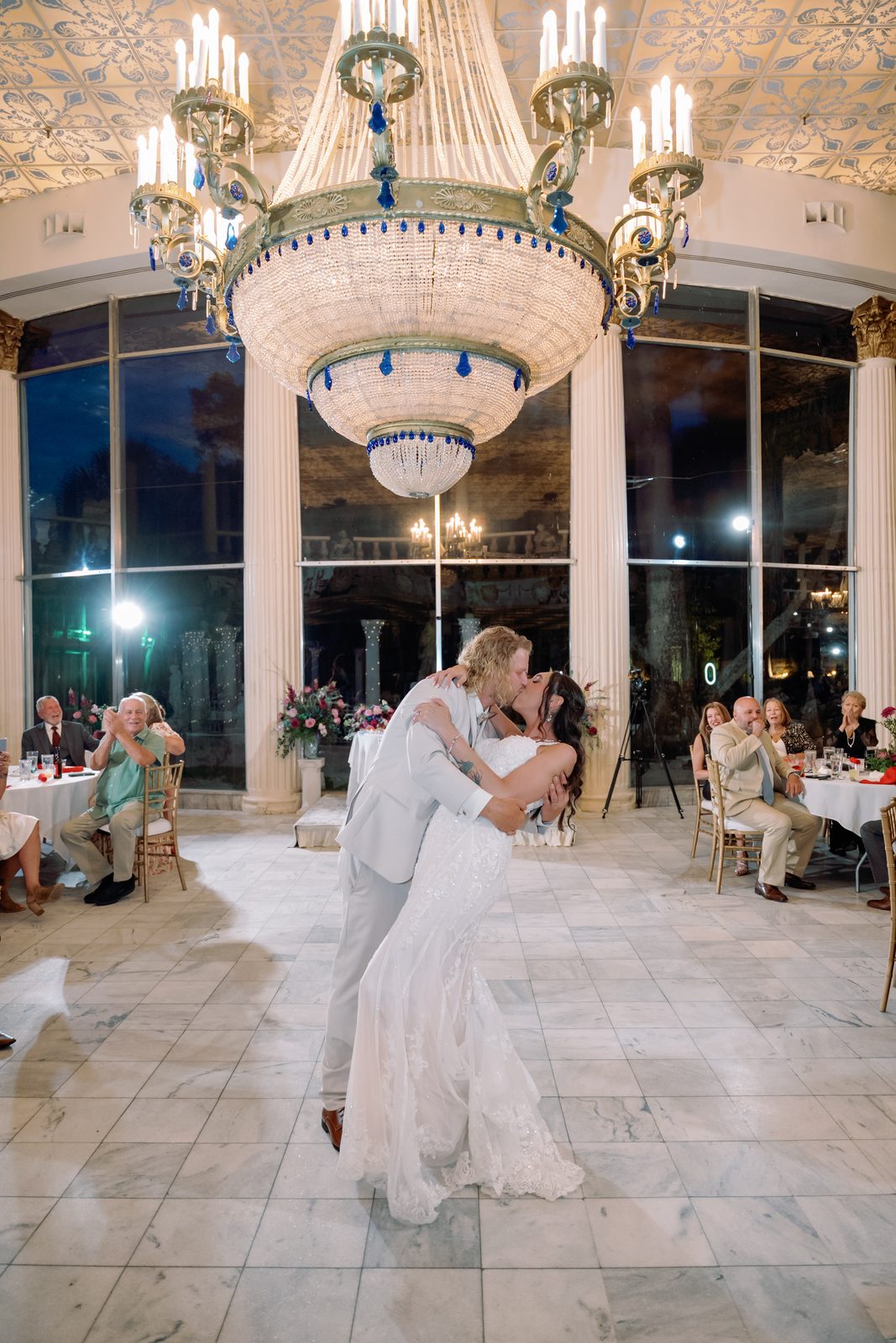 A couple dipping during their first dance beneath a crystal chandelier